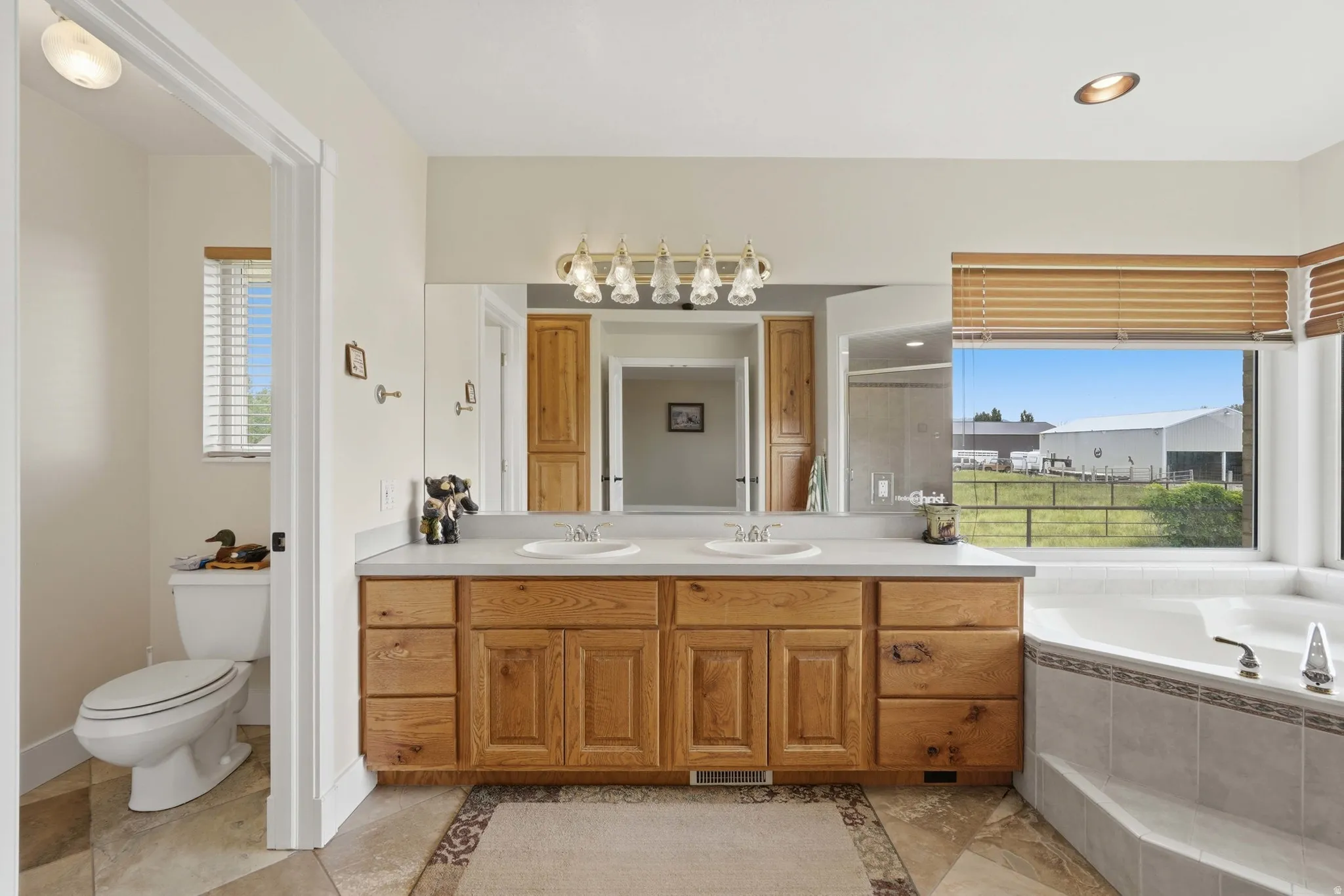 Bathroom featuring a dual vanity with wood cabinetry, a large mirror, and a built-in corner bathtub with tiled surround