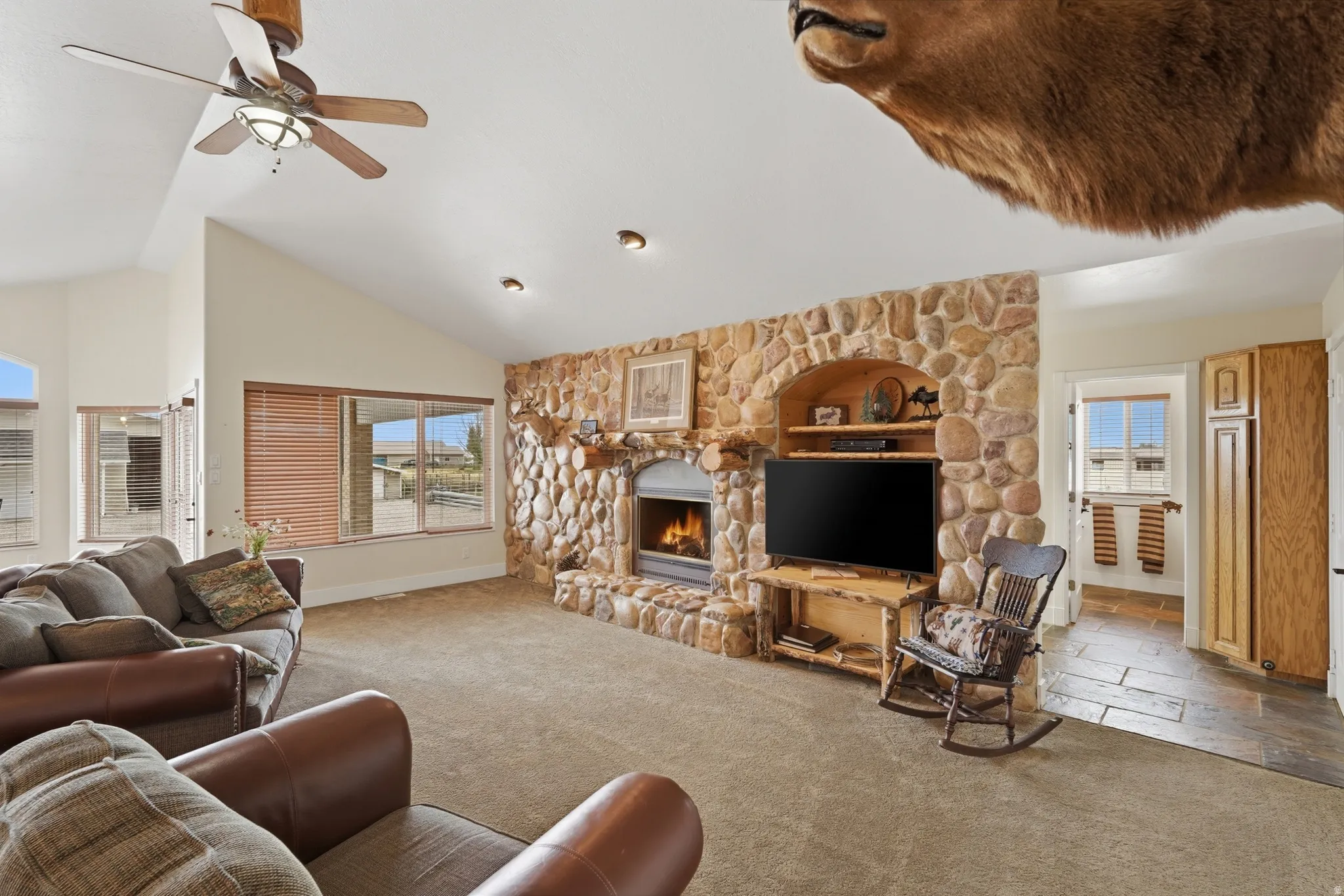 Spacious living area featuring a stone fireplace, integrated shelving, vaulted ceilings, and recessed lighting
