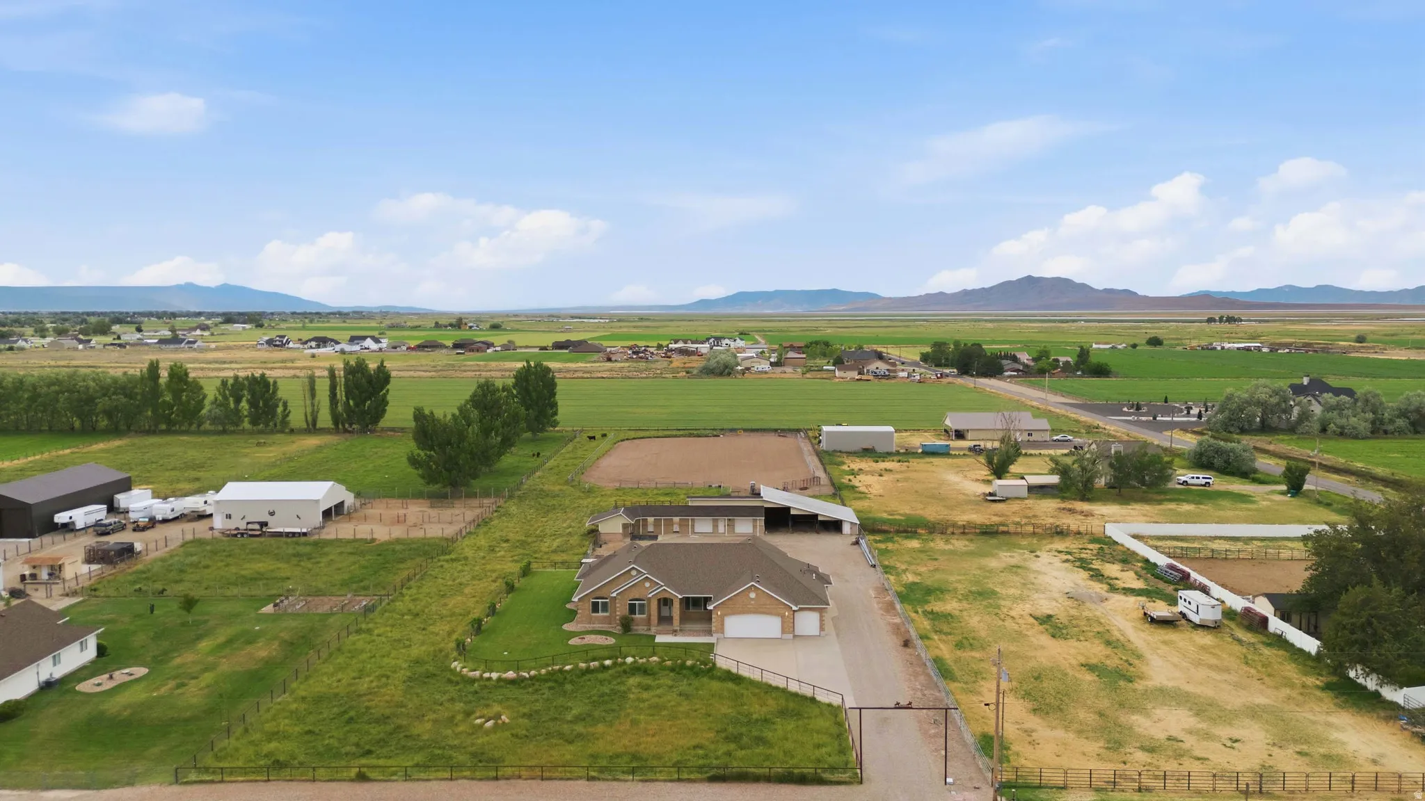 Expansive rural property featuring a main residence with attached garage, multiple outbuildings, fenced pastures, and an outdoor arena
