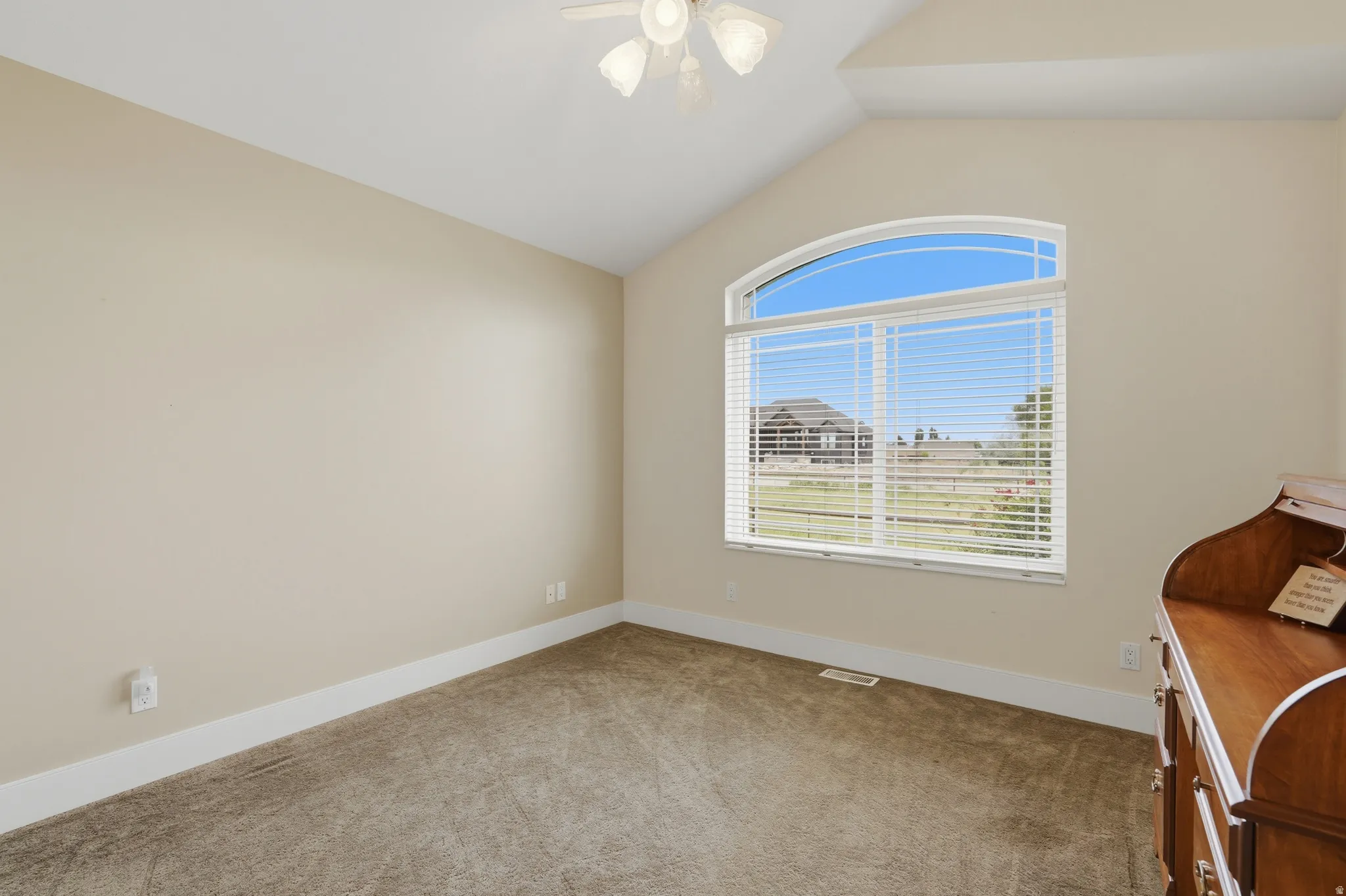 Vaulted ceiling room featuring an arched window, textured carpet flooring, and a ceiling fan with light fixture