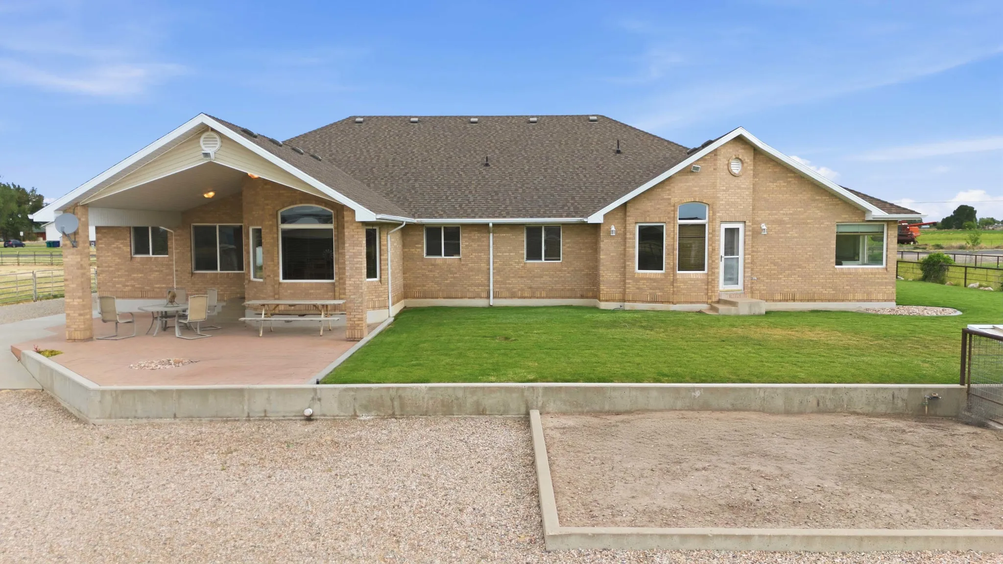 Expansive brick exterior with a covered patio area, large windows, and a manicured lawn