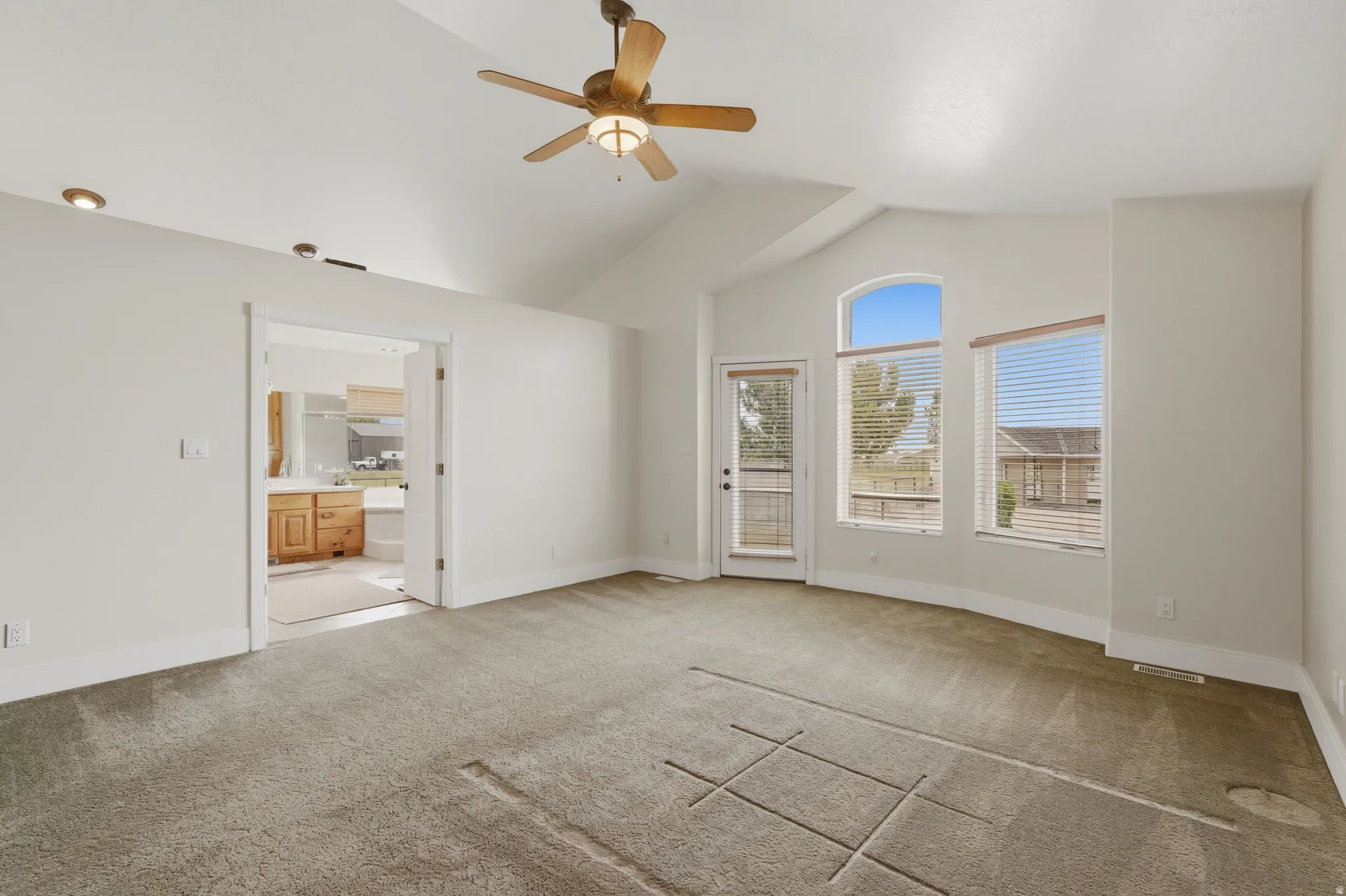 Spacious room featuring vaulted ceilings, a ceiling fan with integrated lighting, recessed lighting, and a glass-paneled exterior door with side windows including an arched transom