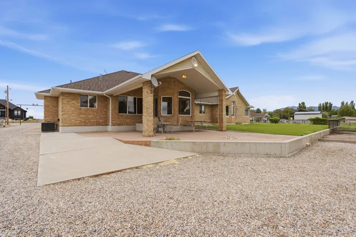 Rear exterior featuring a covered patio, expansive concrete slab, and a gravel surface