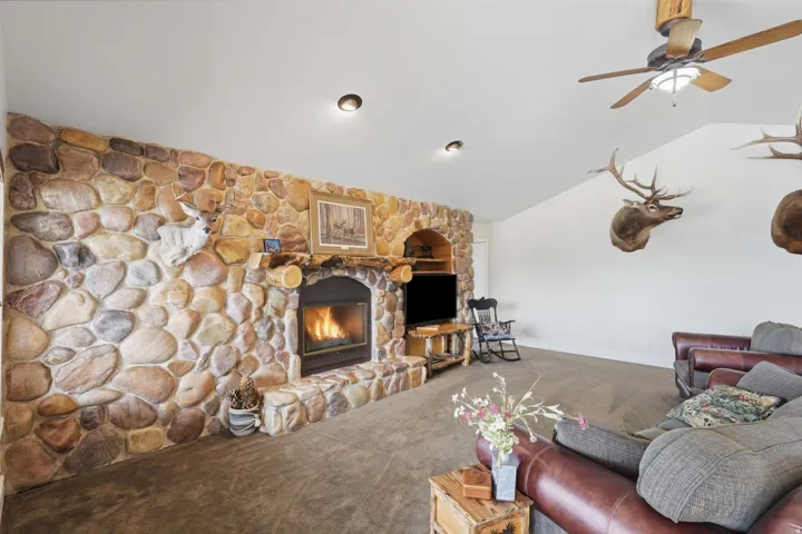 Spacious living area featuring a floor-to-ceiling river rock fireplace with a stone hearth, natural wood mantle, and built-in shelving