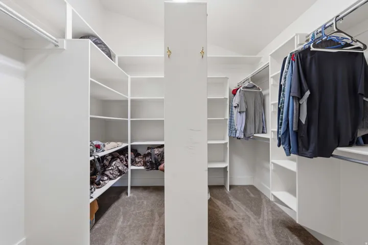 Expansive walk-in closet featuring white built-in shelving, multiple hanging rods, and a central storage column, all set on carpeted flooring