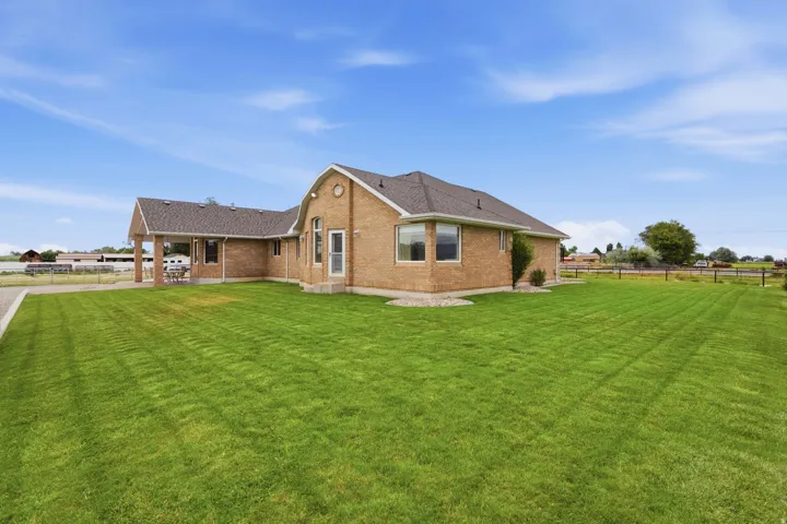Expansive green lawn surrounds a brick residence featuring multiple windows, a covered patio area, and a paved driveway