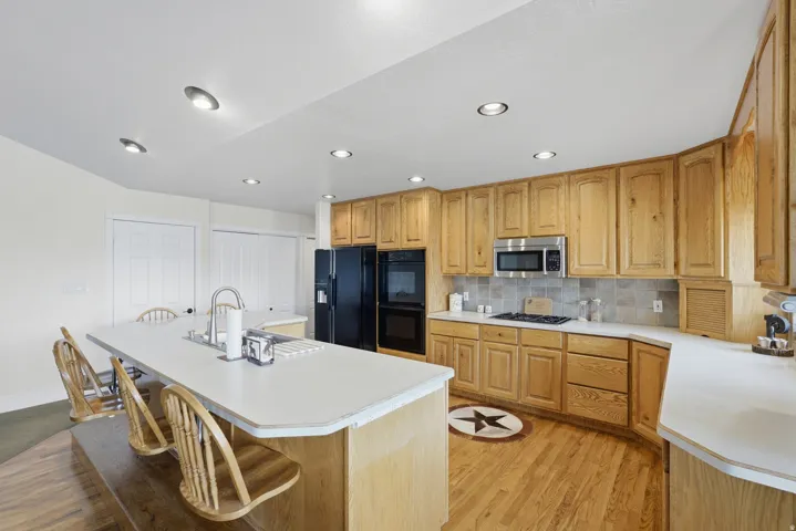Kitchen featuring an expansive island with an integrated sink, ample natural wood cabinetry, a built-in microwave, black appliances, and recessed lighting