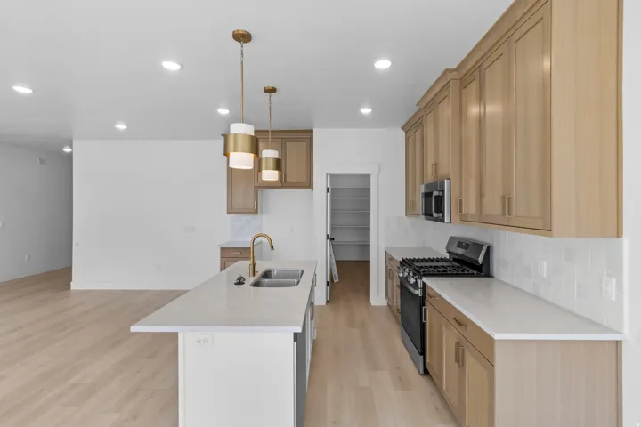 Kitchen featuring light wood-finish cabinetry, a large center island with double basin sink, stainless steel appliances, and recessed lighting