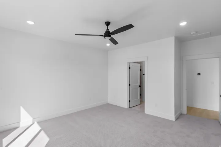 Spacious room featuring light gray carpet, crisp white walls, and a contemporary matte black ceiling fan