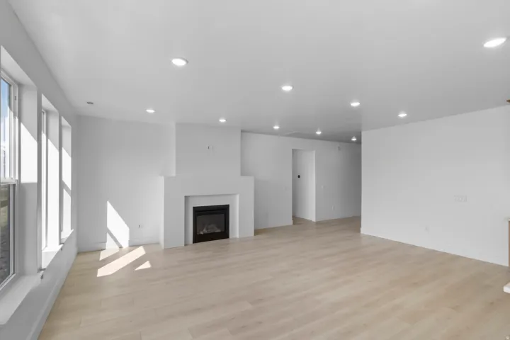 Spacious open-concept room featuring a modern fireplace, wood-finish flooring, recessed lighting, and multiple windows