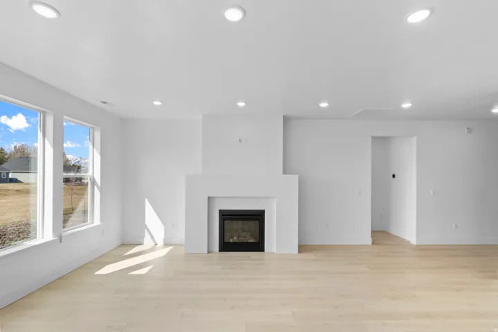 Spacious living area featuring a modern fireplace with a white mantel, light wood-finish flooring, and recessed ceiling lighting