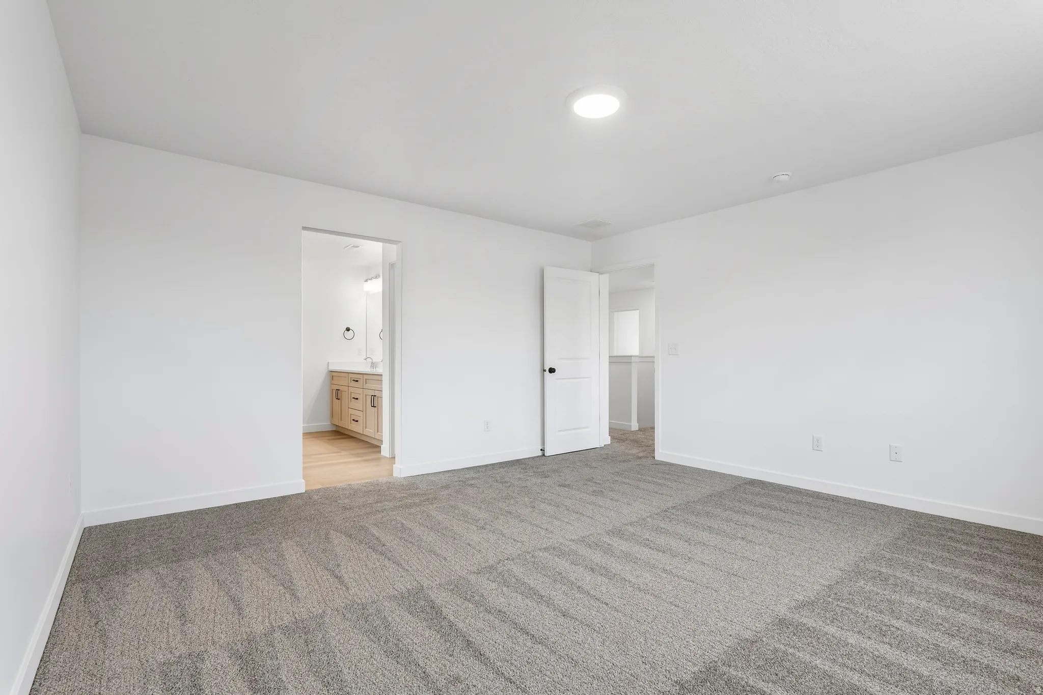 Spacious room featuring neutral grey patterned carpet flooring and bright white walls