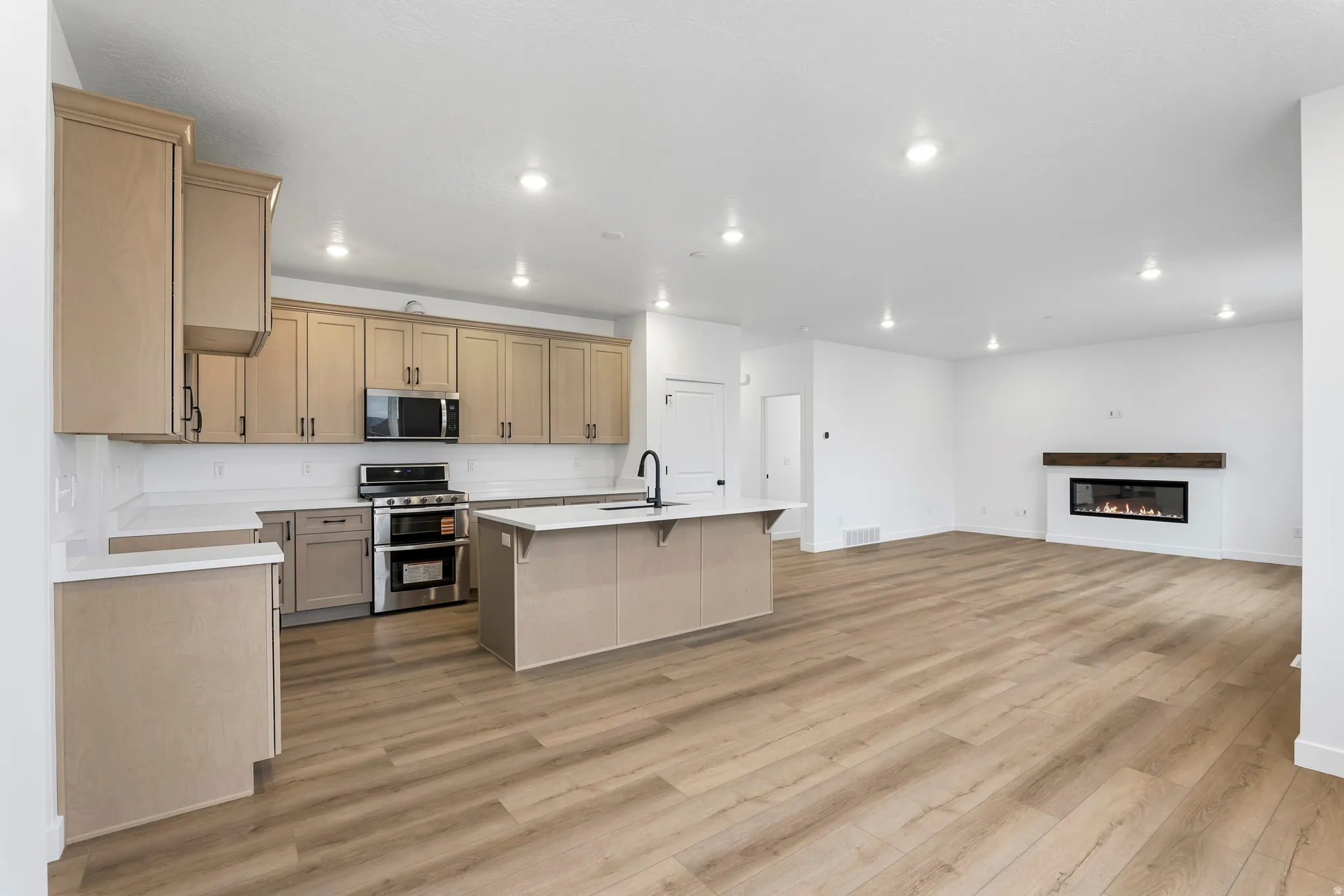 Open-concept living space featuring wood-finish flooring, a contemporary kitchen with light-toned cabinetry, stainless steel appliances, and a central island