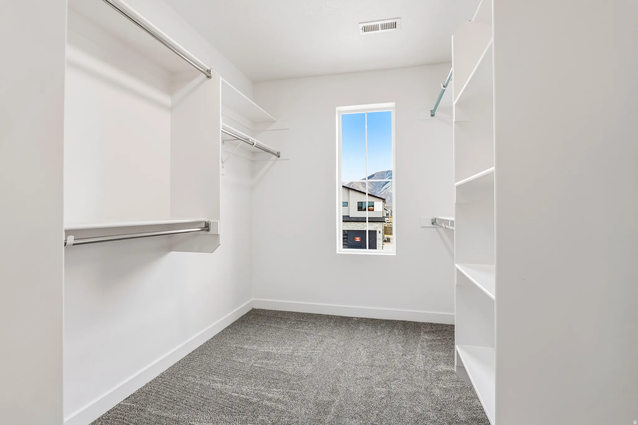 Spacious walk-in closet featuring white built-in shelving, chrome hanging rods, and grey carpet flooring