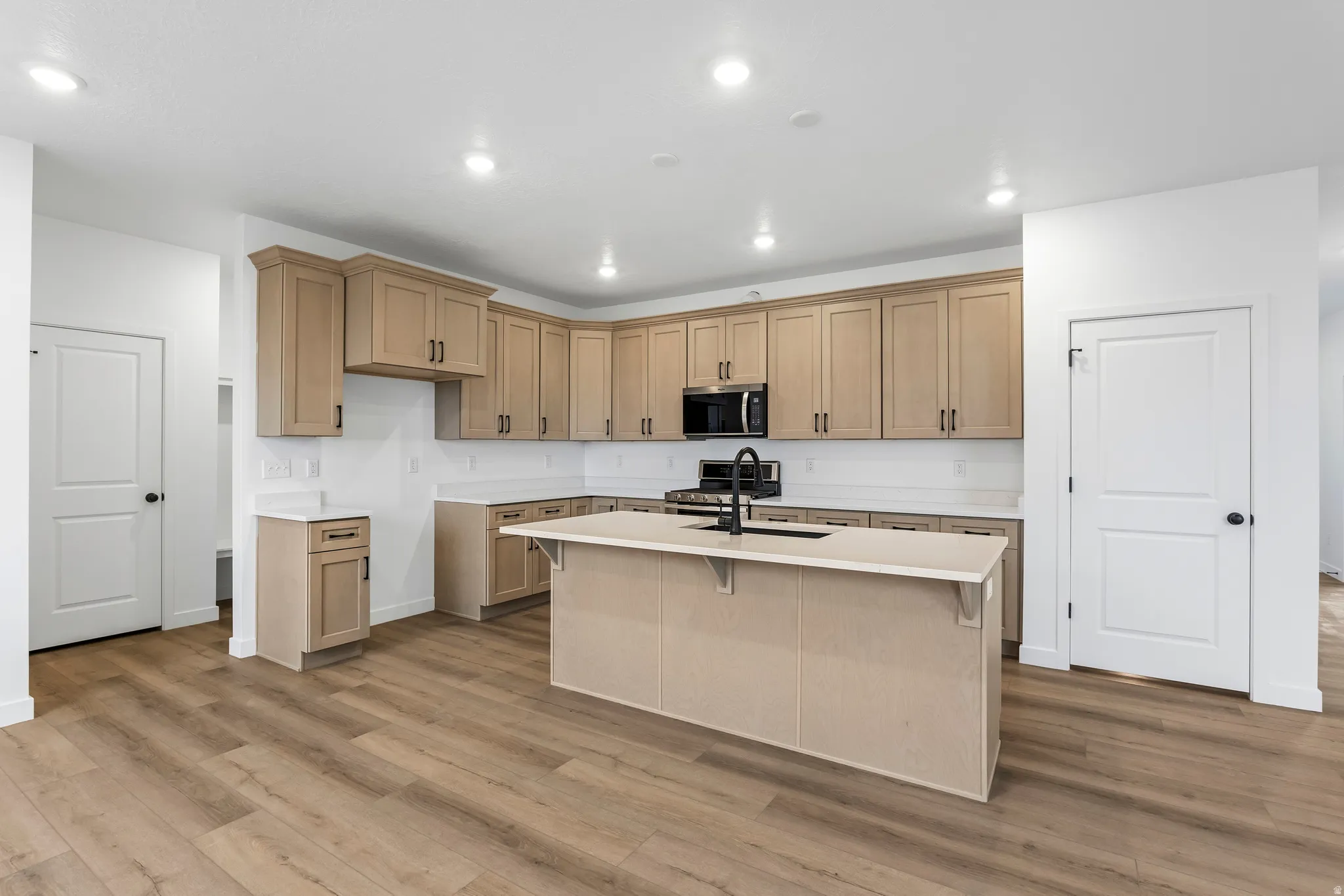 Kitchen featuring wood-finish flooring, recessed lighting, and a central island with an integrated sink and matte black faucet