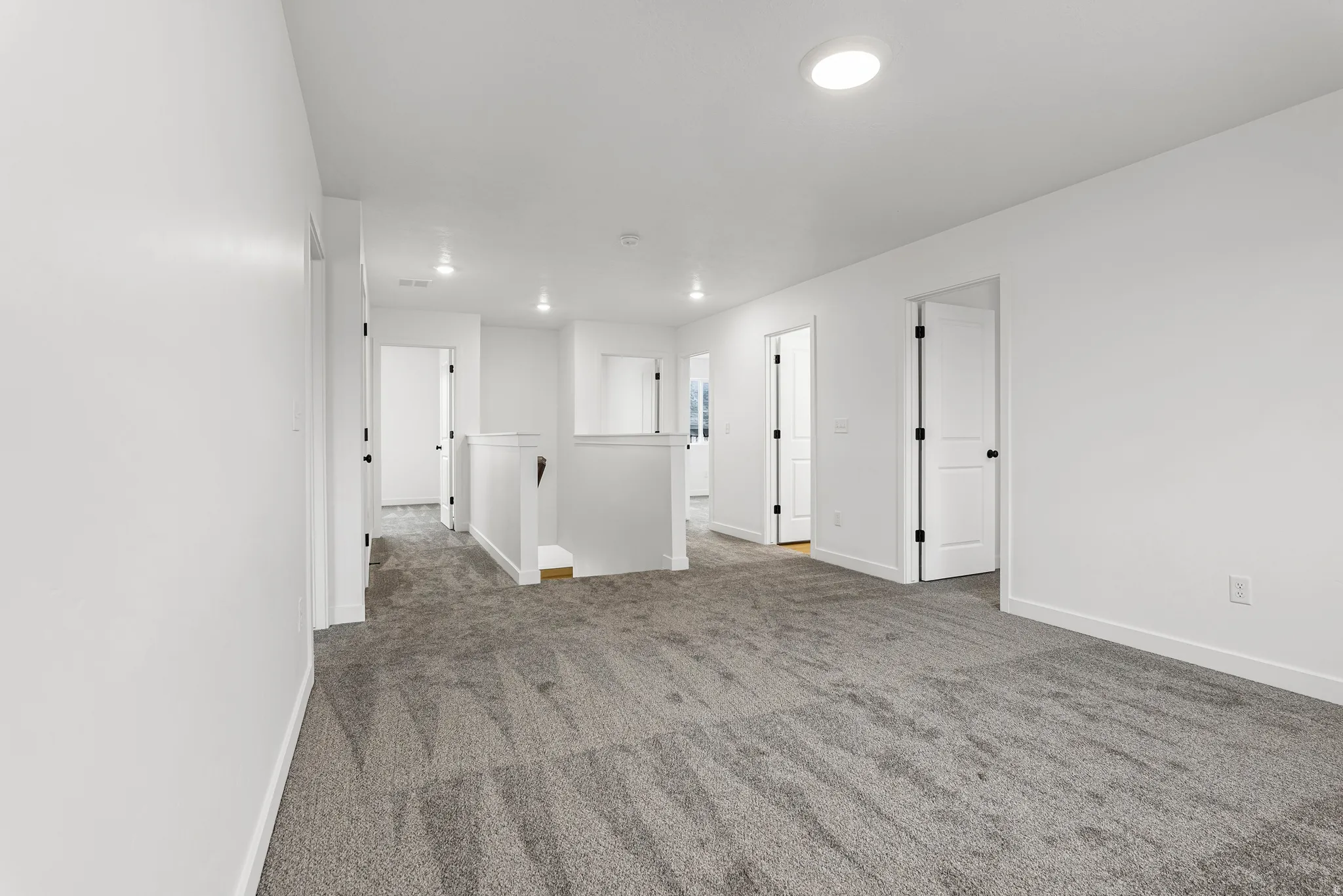 Spacious carpeted landing featuring white walls, recessed lighting, and multiple interior doors with matte black hardware