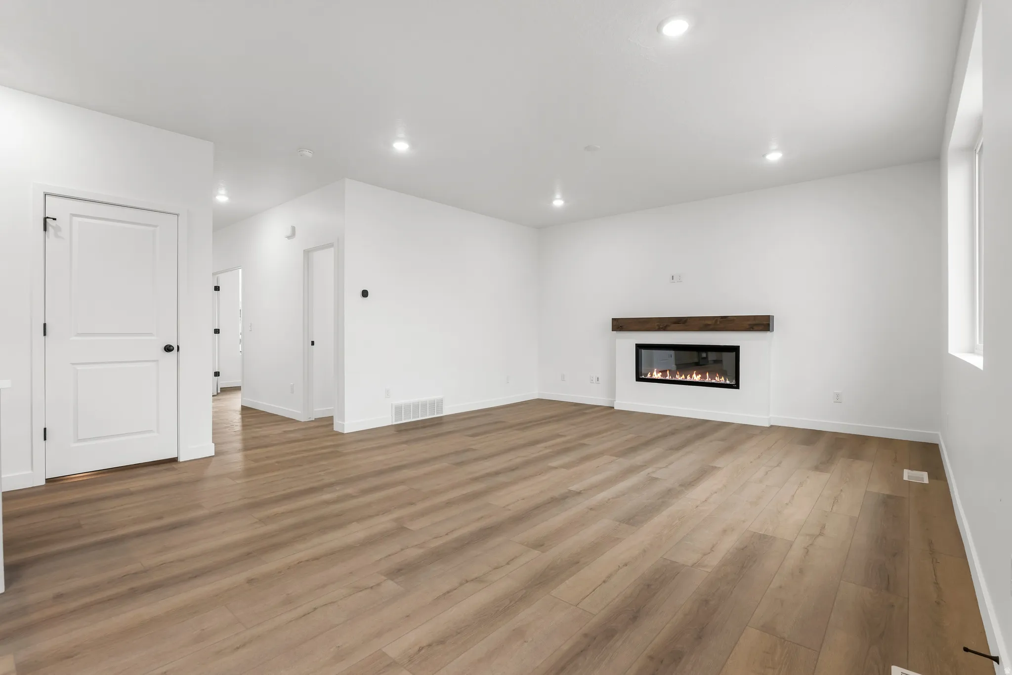 Spacious room featuring wood-finish flooring, recessed lighting, and a modern linear fireplace with a wood mantel