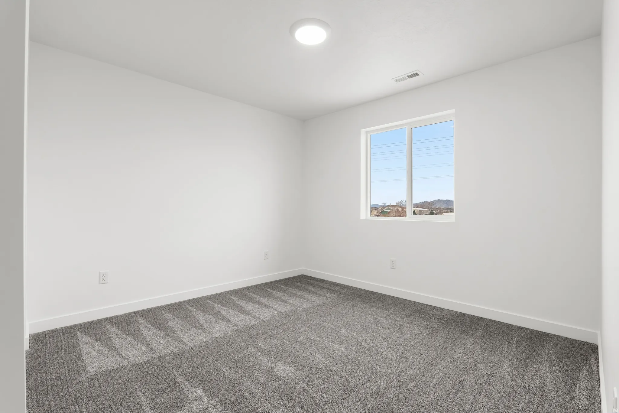 Room featuring a single window, recessed ceiling light, white walls, and grey patterned carpeting