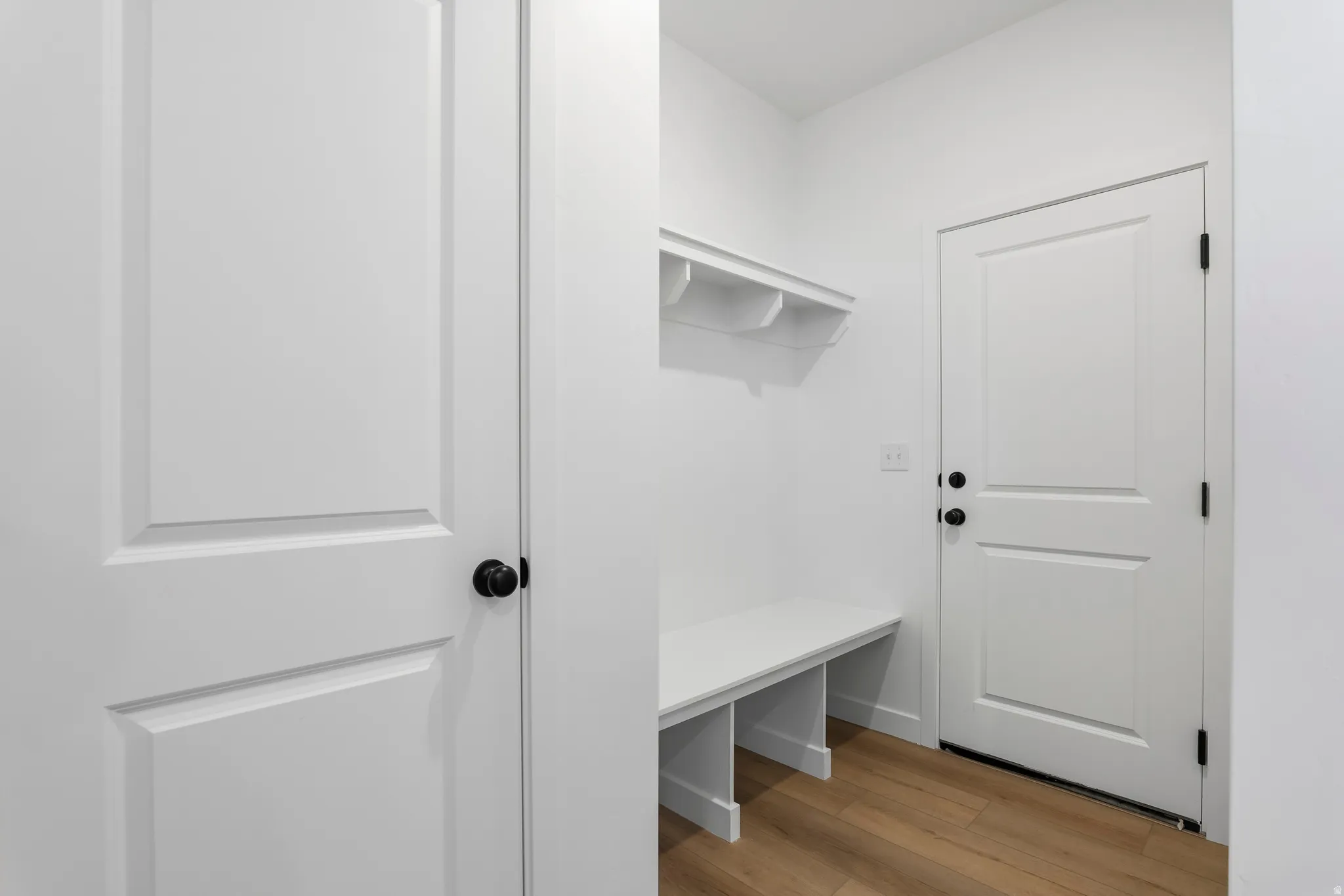 Entryway featuring a built-in bench, wall-mounted shelf with cubbies, white paneled doors, black door hardware, and wood-finish flooring