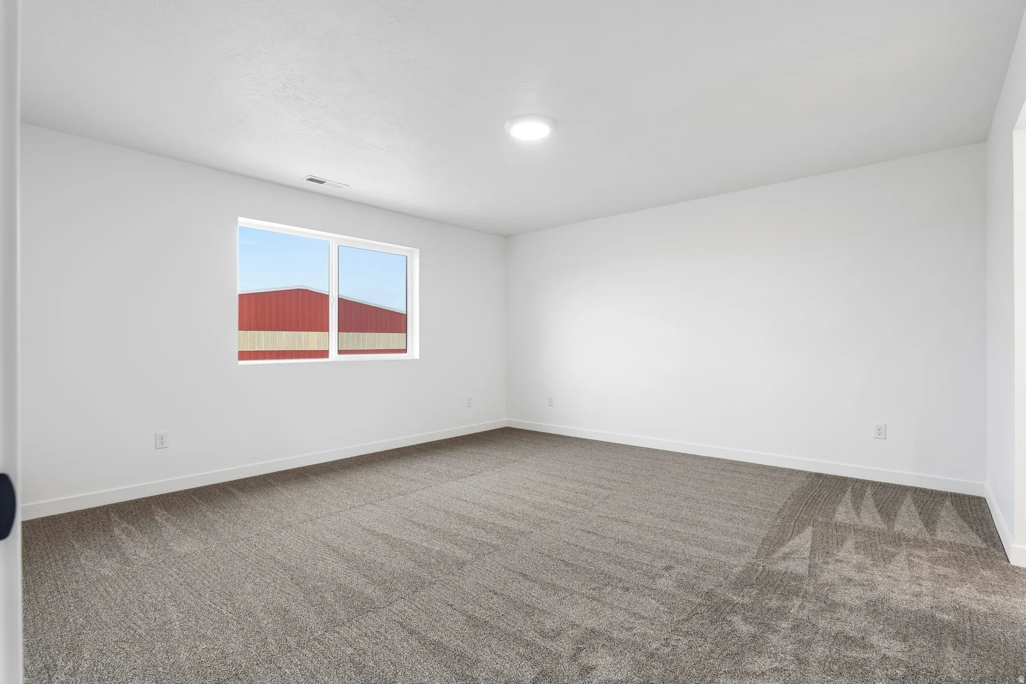Spacious room featuring neutral carpeting, white walls, and a large window