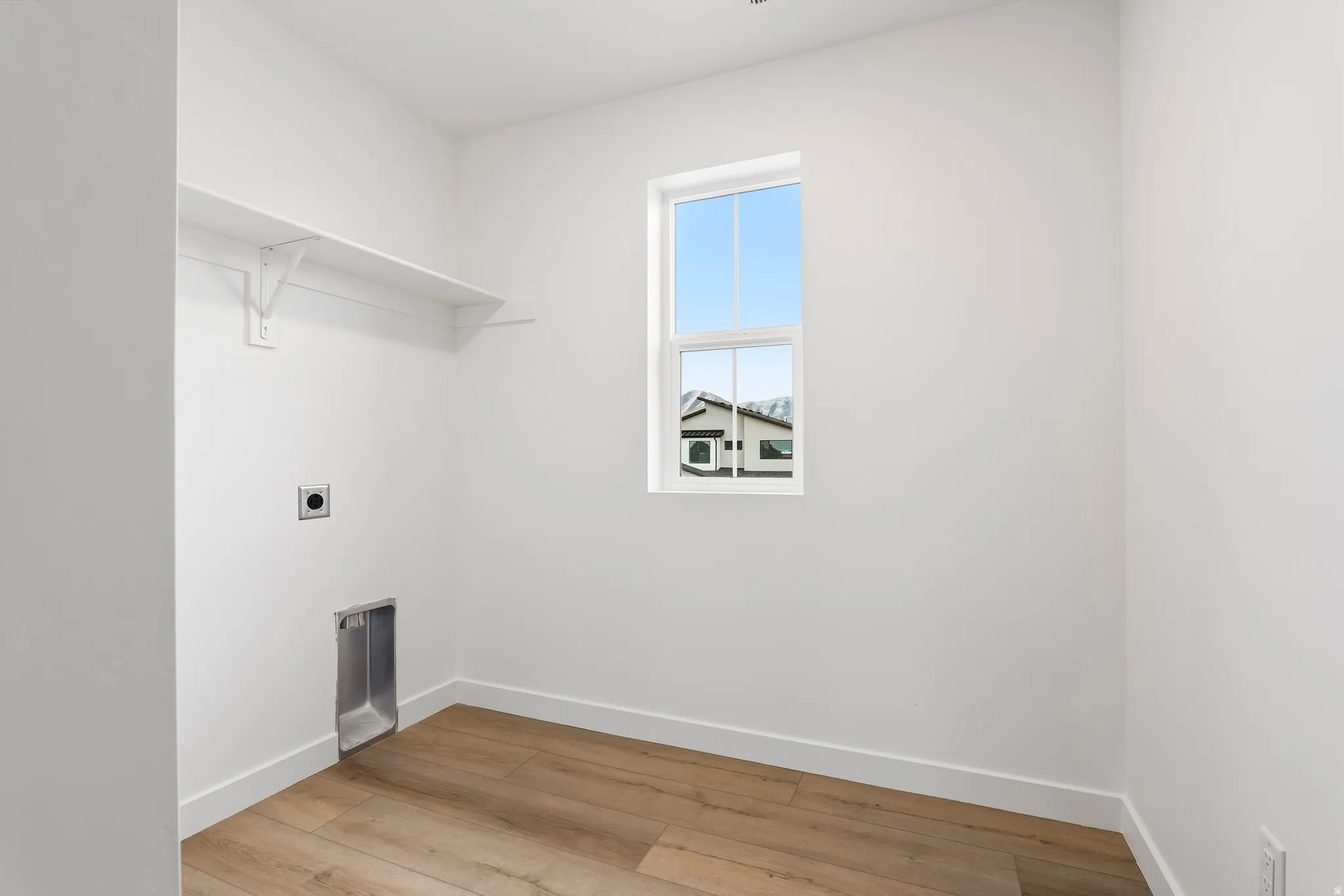 Laundry room featuring wood-finish flooring, white walls, and a single window