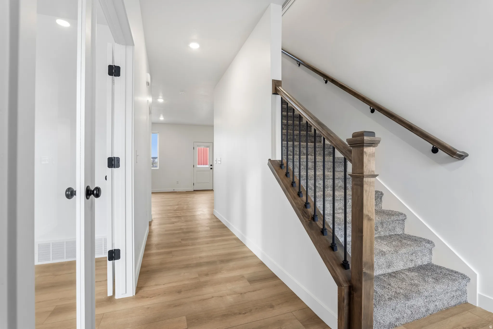 Staircase featuring wood-finish handrails, black metal balusters, and carpeted treads