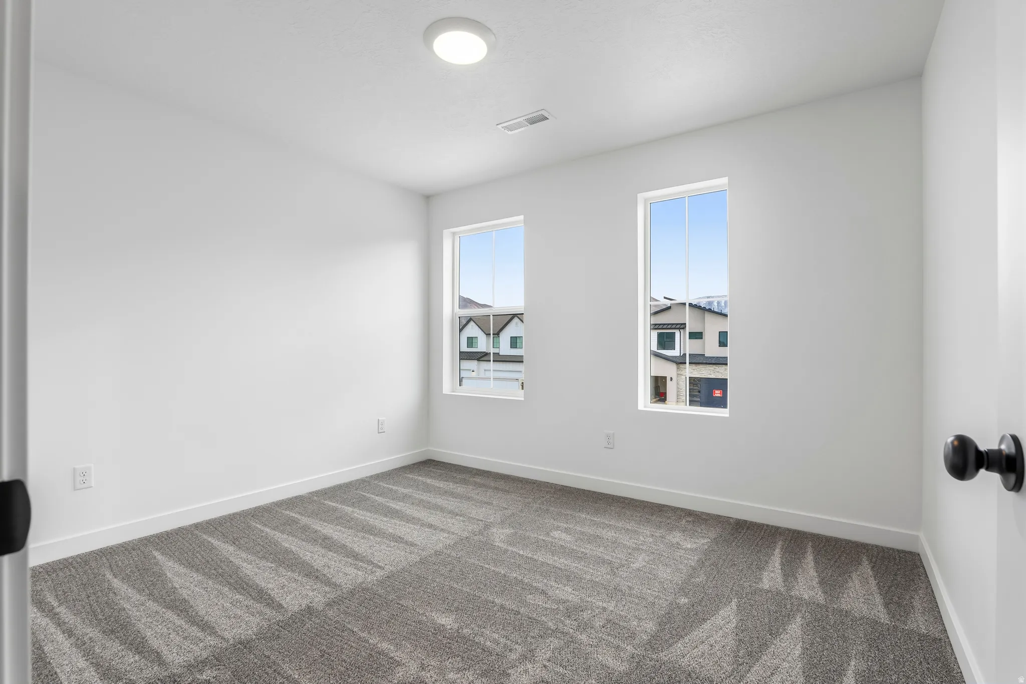 Room with two vertical windows, white walls, and geometric pattern carpeting