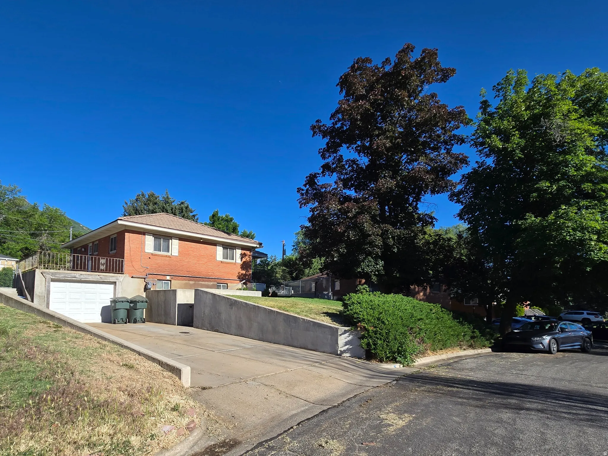 Brick exterior residence featuring a visible garage, concrete driveway, and mature landscaping