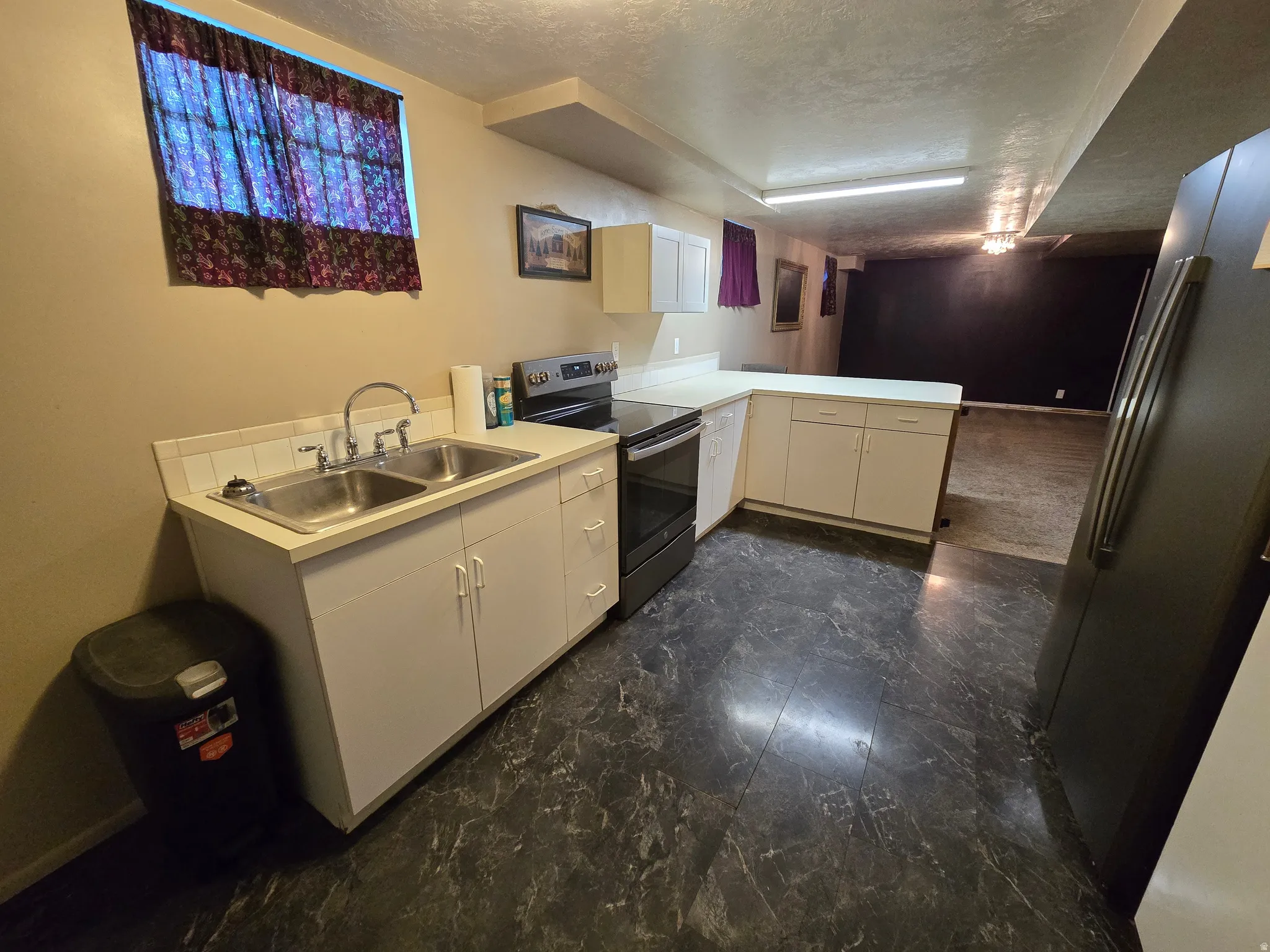 Kitchenette featuring a double basin stainless steel sink, a smooth-top range with an oven, and white cabinetry