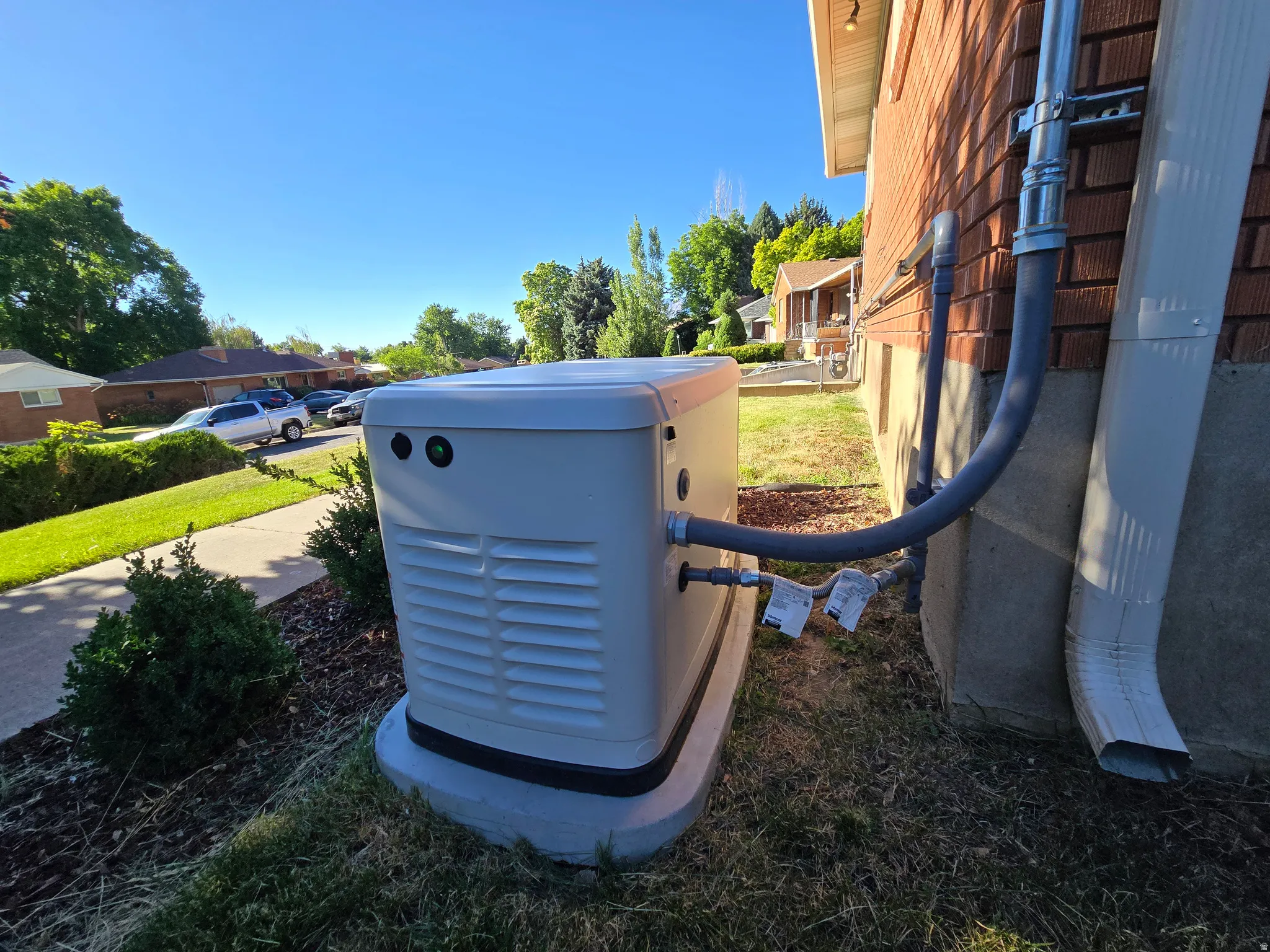 Exterior generator system installed on a concrete pad, featuring utility connections to the brick-sided structure