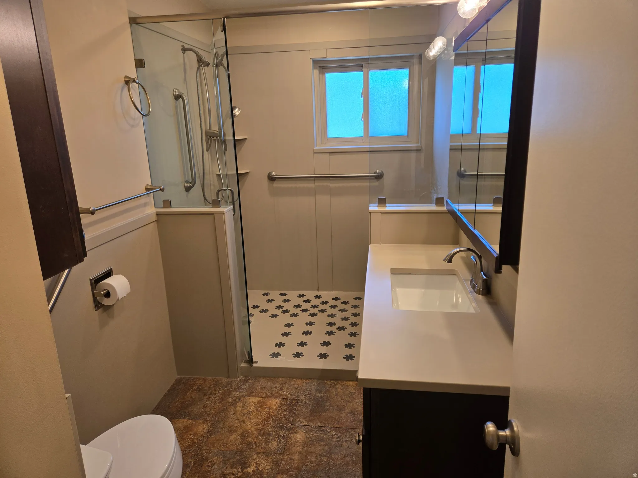Contemporary bathroom featuring a walk-in shower with glass enclosure, decorative mosaic tile shower floor, and a single-pane window