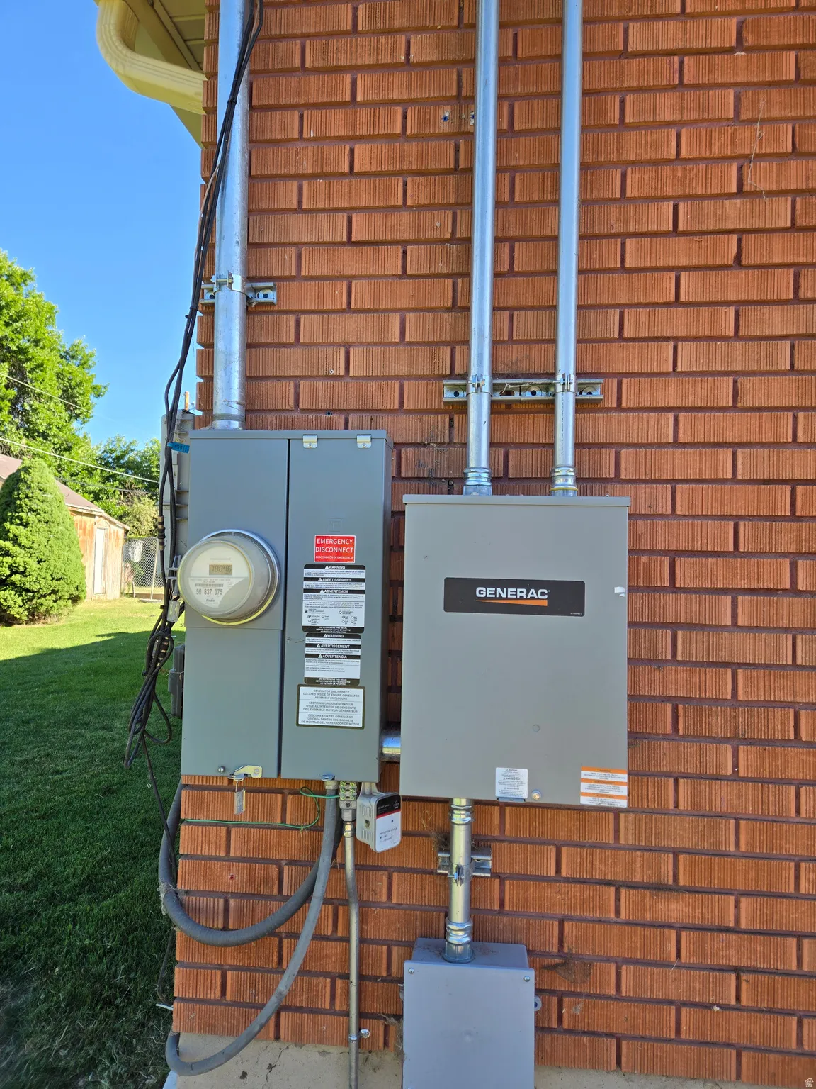 Exterior brick facade featuring a Generac brand generator, utility meter, and galvanized conduit