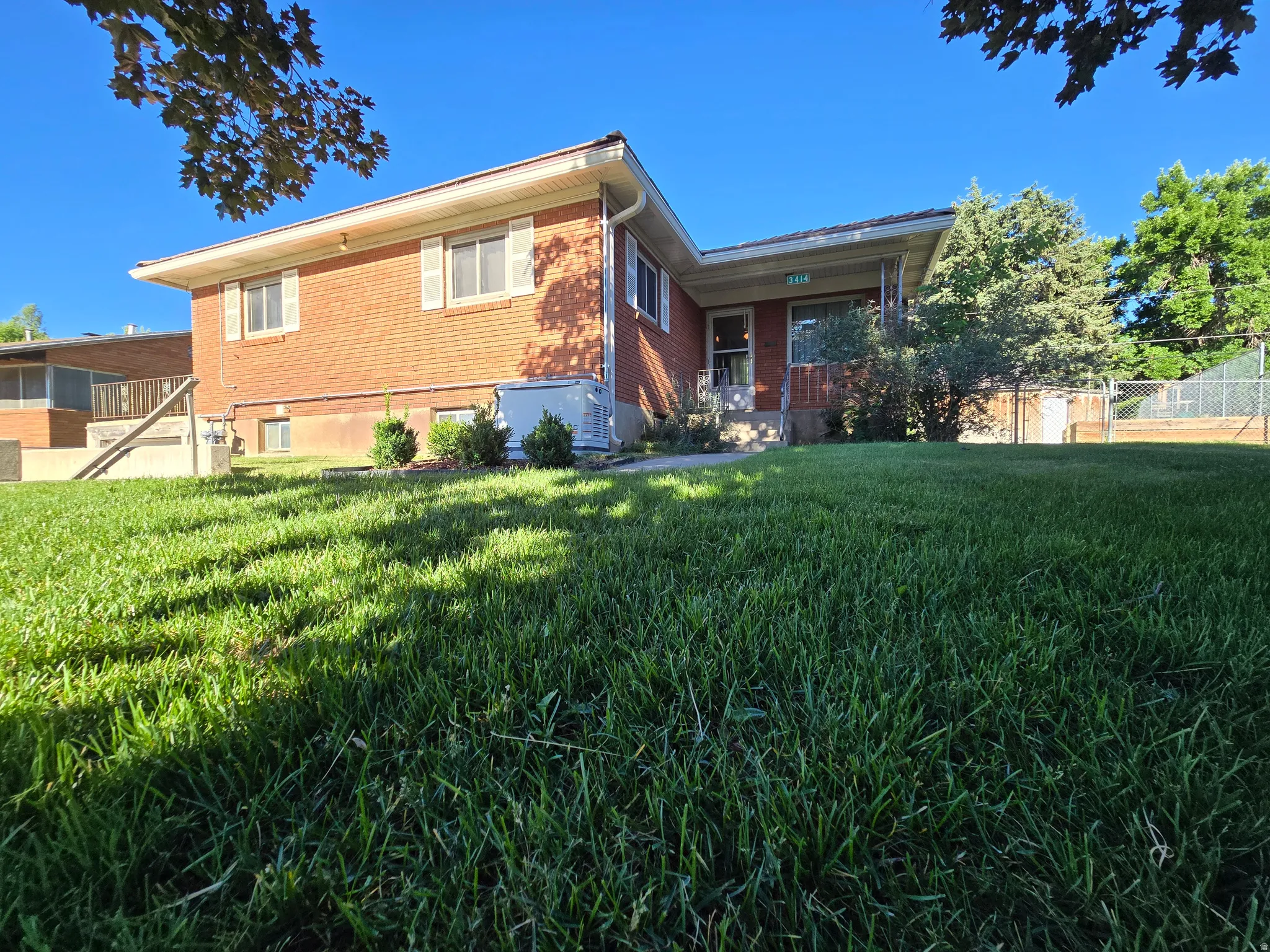 Brick exterior residence featuring white window shutters, a covered front entry, and a sloped lawn
