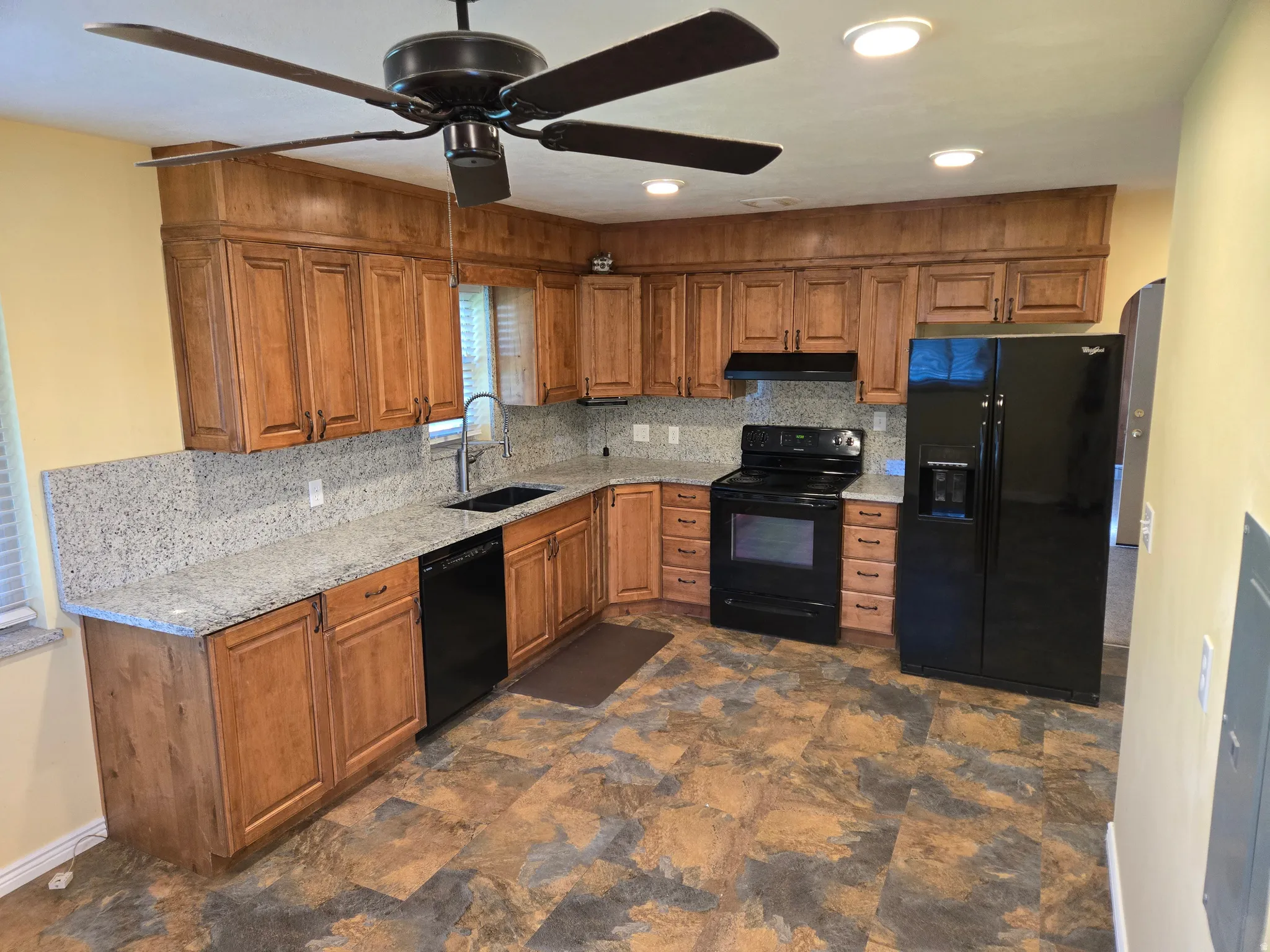 Kitchen featuring wood-finish cabinetry, light-toned speckled countertops, black appliances, a ceiling fan, and recessed lighting