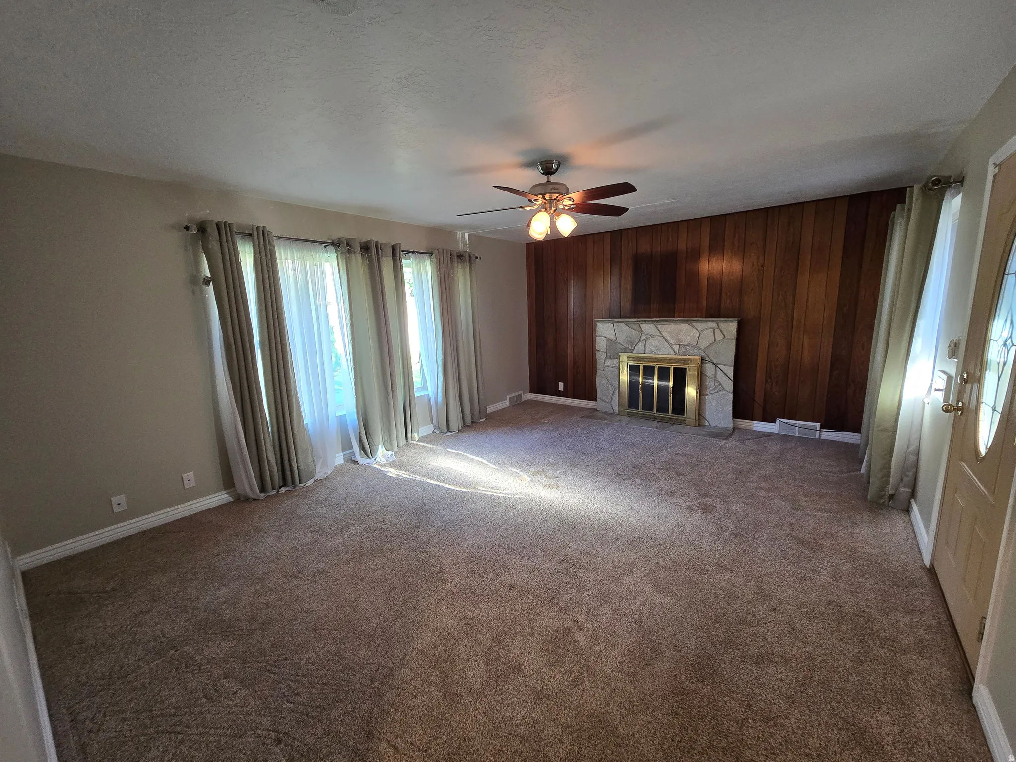 Living area featuring a stone fireplace with a brass firebox, wood-paneled accent wall, and ceiling fan with integrated lighting