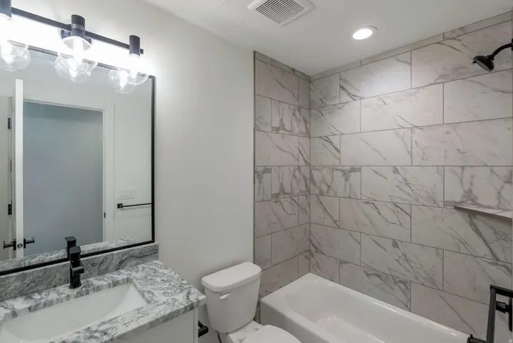 Bathroom featuring a white bathtub, white vanity with a patterned countertop, and a large mirror
