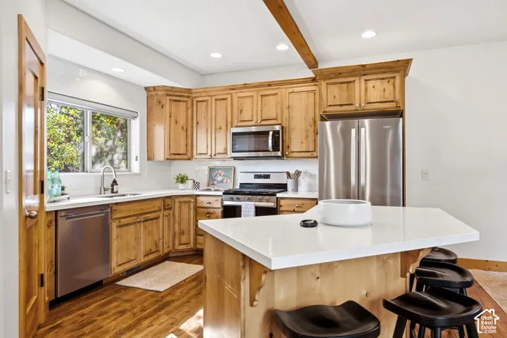 Kitchen featuring wood cabinetry, stainless steel appliances, white subway tile backsplash, and a white countertop island with seating