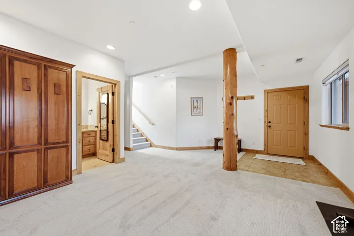 Spacious carpeted area featuring a natural wood support column, light wood paneled entry door, and built-in cabinetry