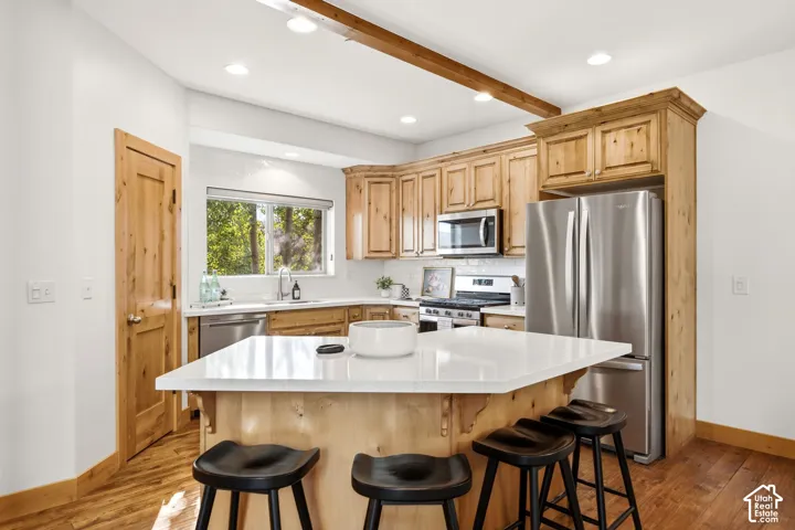 Kitchen featuring a central island with a white countertop, wood-finish flooring, natural wood cabinetry, stainless steel appliances, and recessed lighting