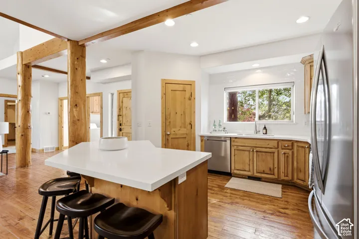 Kitchen featuring a white countertop island, wood-finish flooring, natural wood cabinetry, a stainless steel dishwasher, and a window with white subway tile backsplash