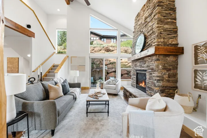 Vaulted ceiling living area featuring a stacked stone fireplace with a substantial wood mantel, large windows, wood-finish flooring, and a staircase with wood handrails