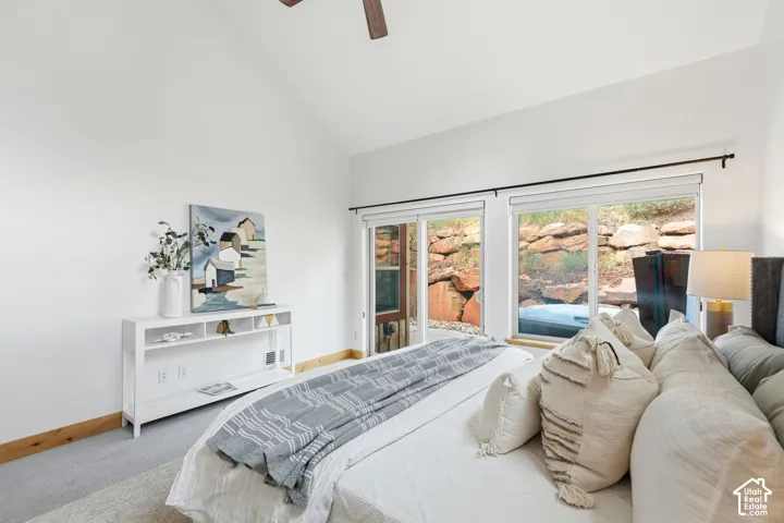 Spacious bedroom featuring vaulted ceilings, a wood-finish ceiling fan, and large sliding glass doors leading to an outdoor spa with natural rock landscaping