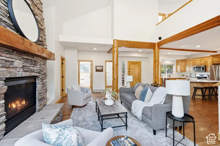 Living area featuring a stone-clad fireplace with a wood mantel, vaulted ceilings, exposed timber beams, and wood-finish flooring