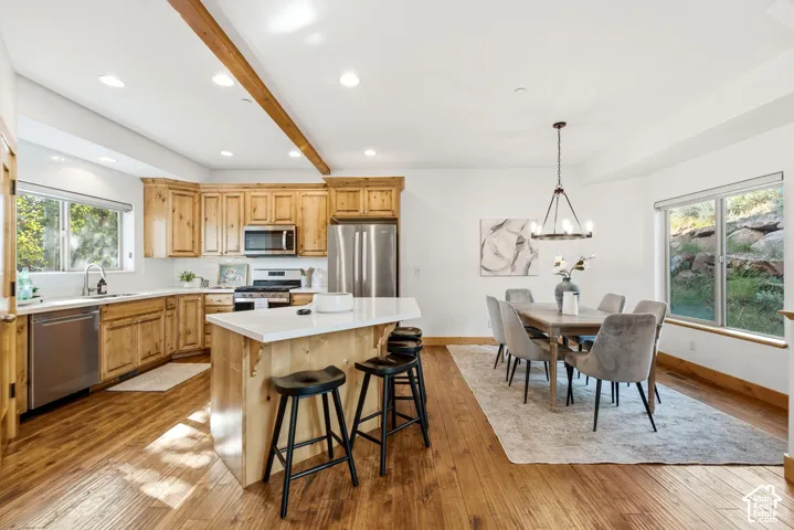 Open-concept kitchen and dining area featuring wood-finish flooring, recessed lighting, and a visible wood beam