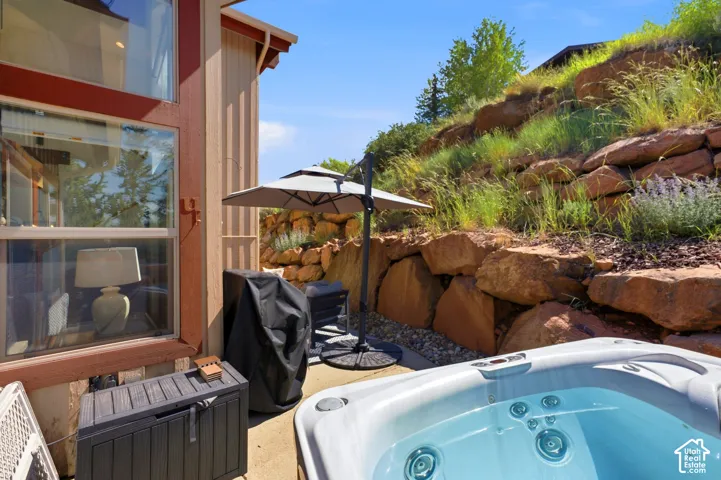 Outdoor patio featuring an inground hot tub, concrete paving, and a retaining wall constructed from large natural stone blocks