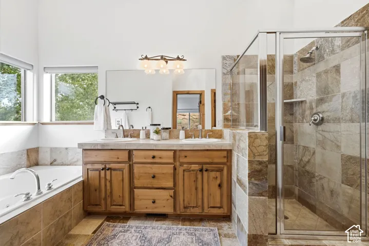 Bathroom featuring a dual vanity with wood cabinetry, a built-in soaking tub, a glass-enclosed shower with tiled walls, and high ceilings