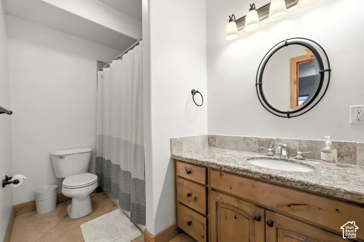 Bathroom featuring a wood-finish vanity with a granite countertop, undermount sink, and a circular framed mirror