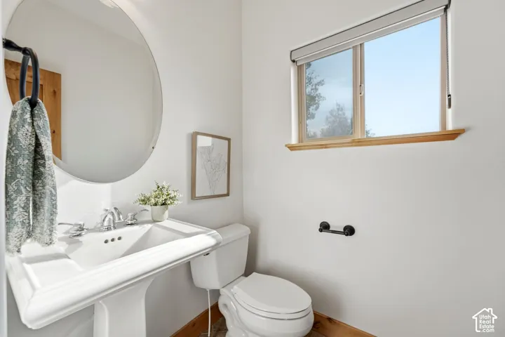 White pedestal sink with chrome faucet hardware, round frameless mirror, and a window featuring a wood-finish sill
