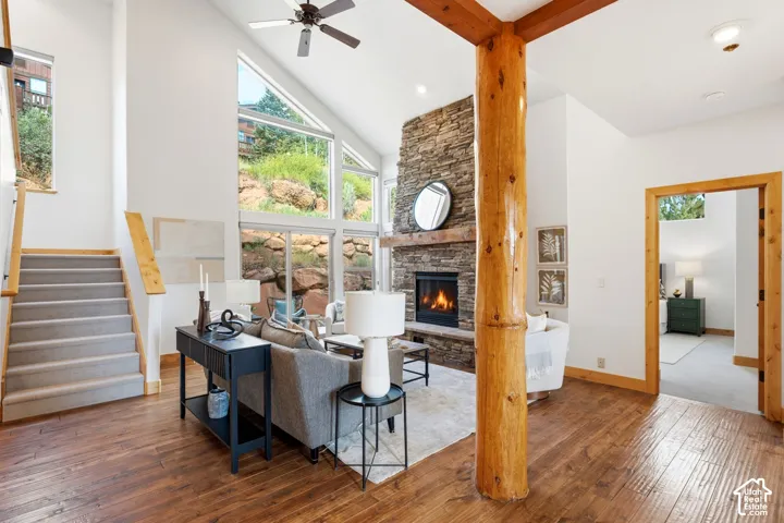 Spacious living area featuring a vaulted ceiling with a ceiling fan, a stone fireplace, and large windows