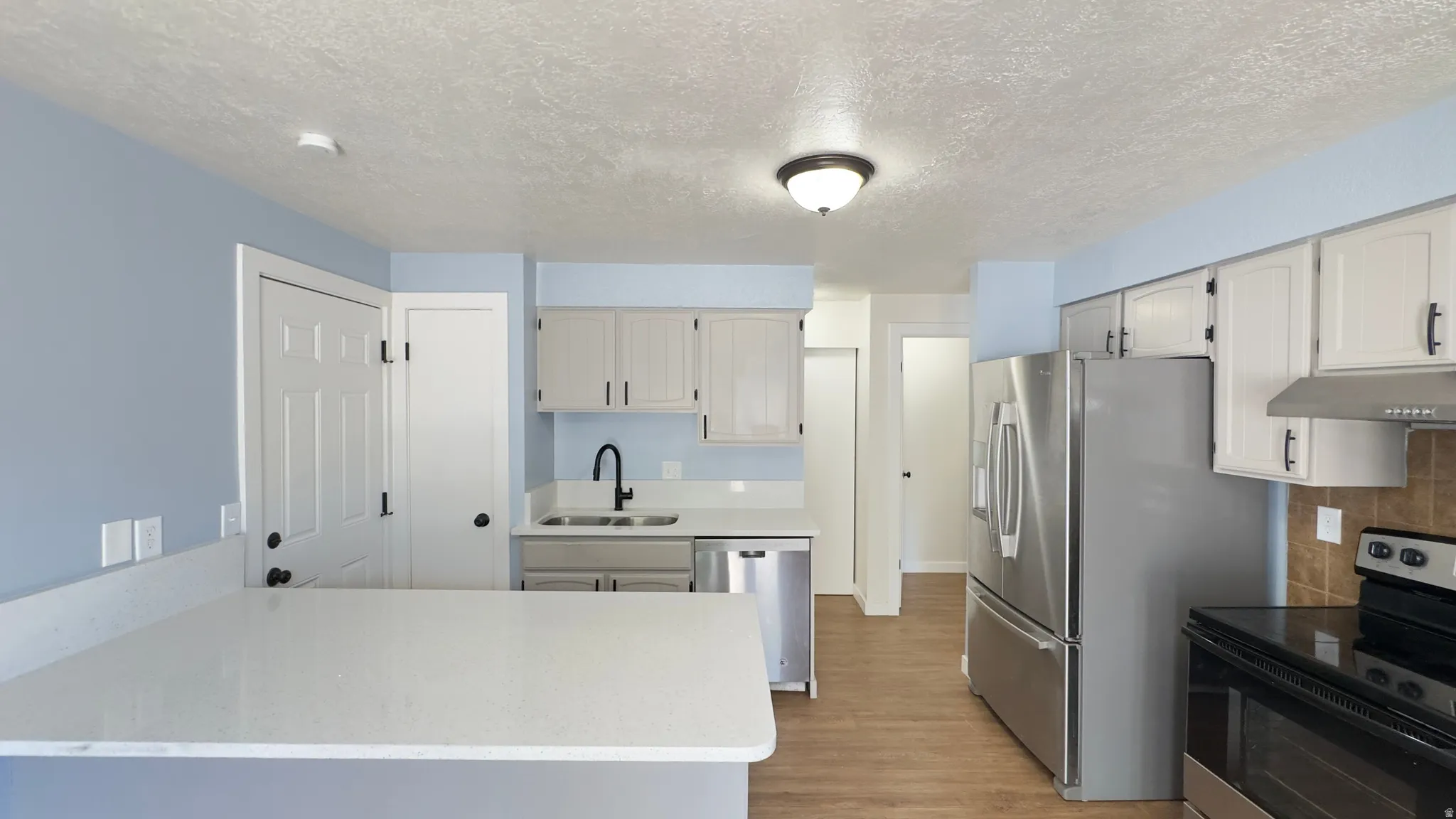 Kitchen featuring white shaker-style cabinetry, stainless steel appliances, a premium white corian countertops, and wood-finish flooring.